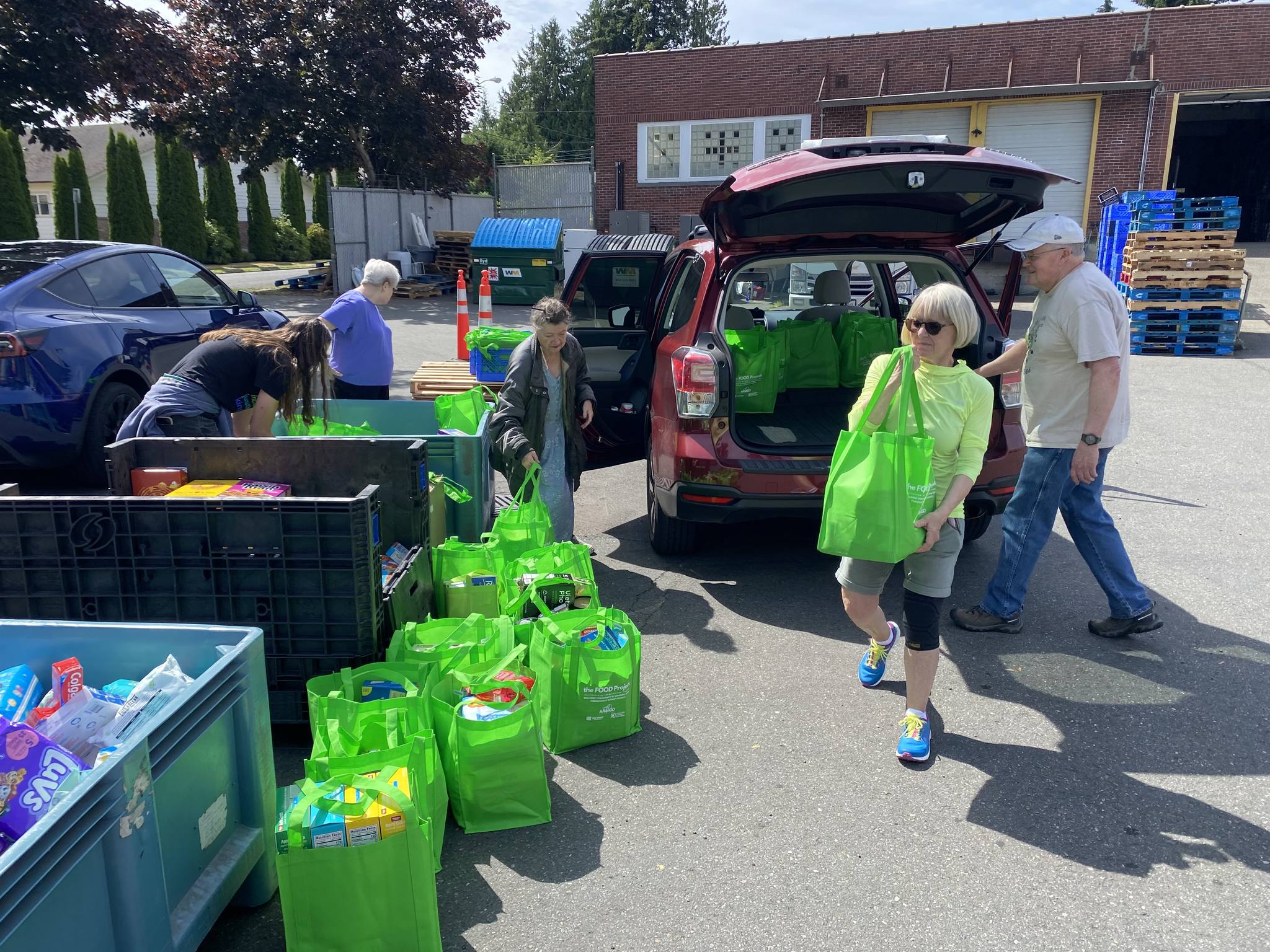 Volunteers unloading green bags of donated groceries at a food drive